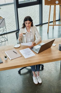 A businesswoman sits with a laptop in a modern office, working on franchising concepts and strategies. clipart