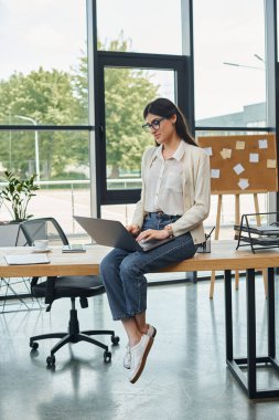 Modern bir ofisteki bir iş kadını masanın üzerine oturur ve özenle dizüstü bilgisayarı üzerinde çalışır..