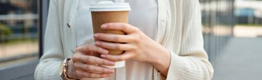 A businesswoman enjoys a quiet moment holding a cup of coffee in a modern outdoor office setting. clipart