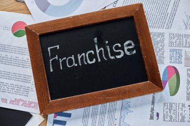 A blackboard with the word franchise written on it in bold chalk, symbolizing business expansion and growth in a modern office setting. clipart