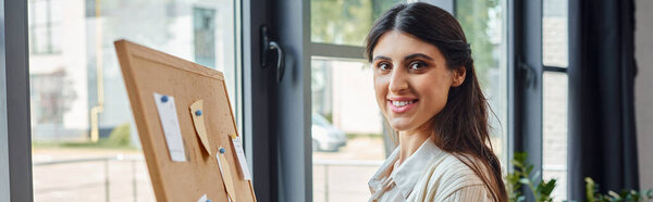 A businesswoman stands poised in front of a wooden board, fully immersed in her artistic endeavor within a modern office workspace.