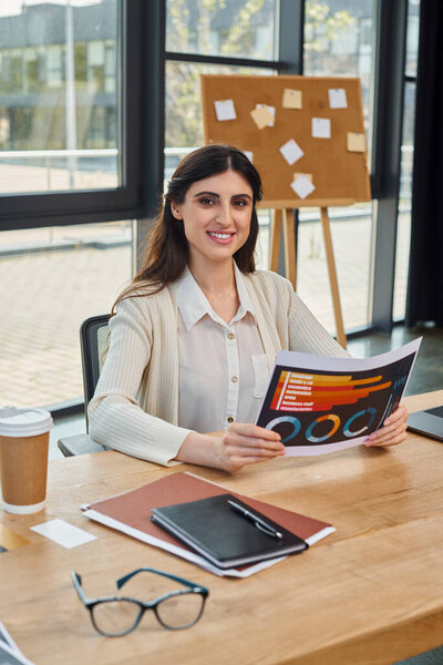 A businesswoman in a modern office, sitting at a table, immersed in reading charts near her workspace, embodying the franchise concept.
