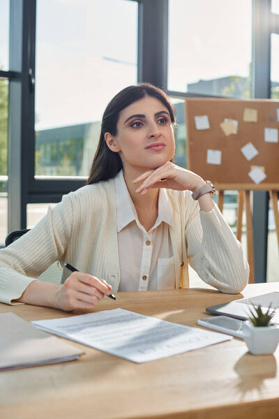 A focused businesswoman sits at a modern office table holding a pen, immersed in the franchise concept work.