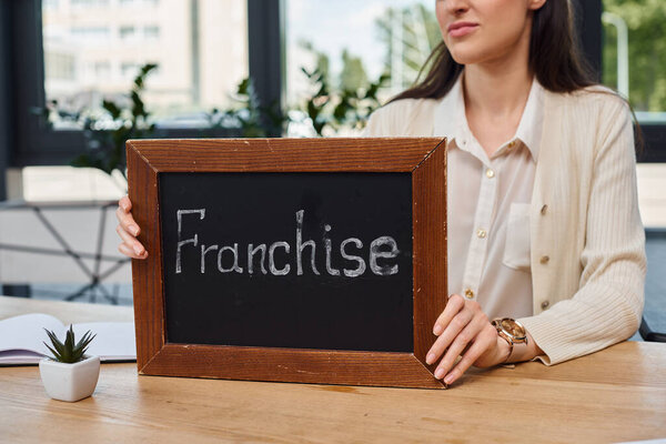 A businesswoman in a modern office sits at a table, holding a sign.