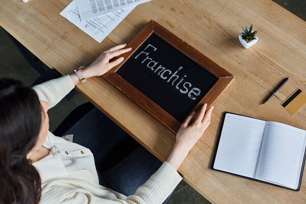 A modern businesswoman sits at a table with a sign of franchise in a contemporary office setting