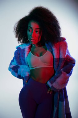 Seksi afro-amerikan kadın canlı sahte kürklü ve sütyenli kırmızı ve mavi ışıklara bakıyor.