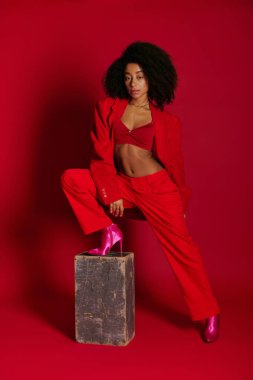 Oldukça modaya uygun bir Afro-Amerikan kadın modeli seksi giyinmiş kırmızı arka planda kameraya bakıyor.