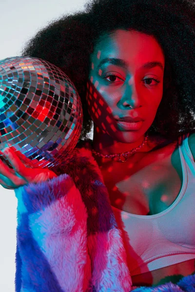 stock image beautiful stylish african american woman in faux fur posing with disco ball and looking at camera