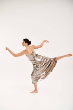A young woman in a silver dress gracefully dances in a studio setting against a white background. clipart