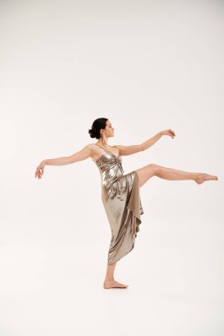 A young woman exudes grace and elegance as she dances in a long, shiny silver dress in a studio setting against a white backdrop. clipart