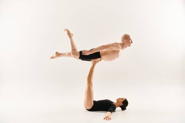 Shirtless young man and woman in black performing acrobatic elements. clipart