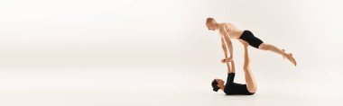 Shirtless young man and woman performing synchronized handstands in a studio setting against a white background. clipart