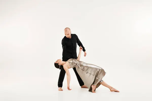stock image A young man in black and a young woman in a dress dance as a couple, incorporating acrobatic elements. Studio shot on a white background.