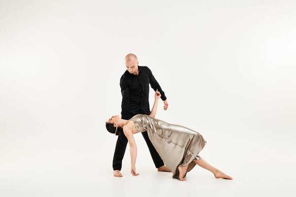 A young man in black and a young woman in a dress dance as a couple, incorporating acrobatic elements. Studio shot on a white background.