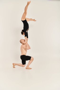 Young shirtless man and woman execute a flawless handstand in mid-air against a white studio backdrop. clipart