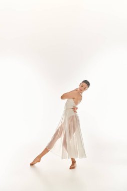 A young woman gracefully dances in a long white dress, exuding elegance and poise in a studio setting against a white background. clipart