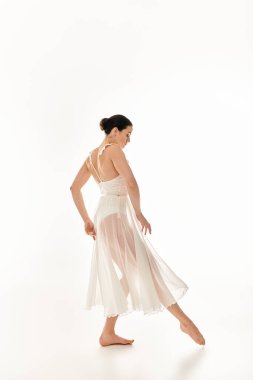 Dalgalı beyaz elbiseli genç bir kadın beyaz bir arka planda zarif bir şekilde dans eder..