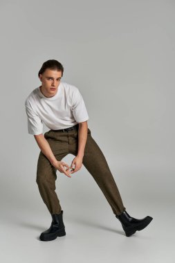 Zarif giyinmiş, kahverengi pantolonlu çekici, sofistike bir adam poz verip kameraya bakıyor.