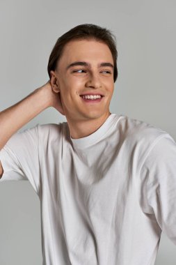 cheerful good looking man in simple t shirt posing alluringly on gray backdrop and looking away clipart