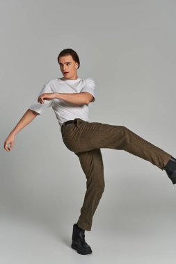 Şık giyinmiş yakışıklı, zarif bir erkek model. Hareket halinde poz veriyor ve gri arka plana bakıyor.