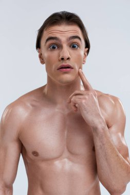 shirtless handsome shocked man posing with finger near face and looking at camera on gray backdrop clipart