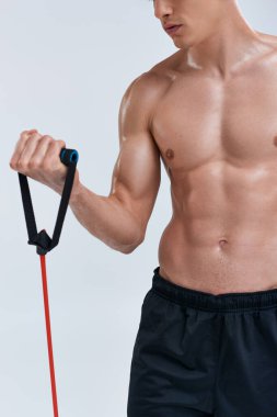 Genç atletik gömleksiz adam eğitimi gri arka planda fitness genişletici