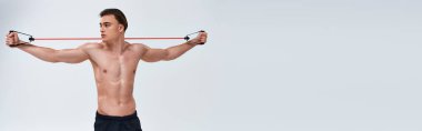 Baştan çıkarıcı, siyah pantolonlu, spor pantolonlu, fitness genişletme antrenmanı yapan ve başka tarafa bakan, afiş giymiş, üstsüz bir adam.