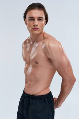 Çekici, seksi, üstsüz, siyah spor pantolonlu, çekici bir şekilde kameraya bakan bir adam.