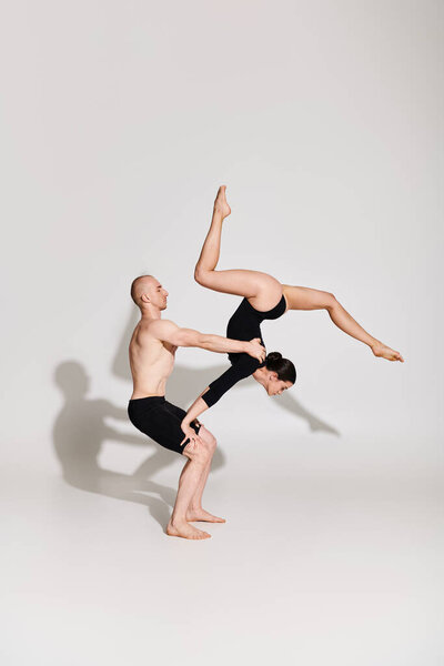Shirtless man and woman perform synchronized handstand in captivating acrobatic display against white backdrop.