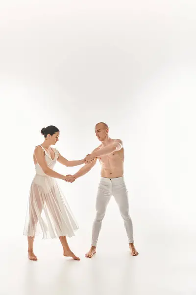 白いドレスで踊る若いシャツのない男と若い女性が 白い背景のスタジオでアクロバティックな要素を実行します — ストック写真