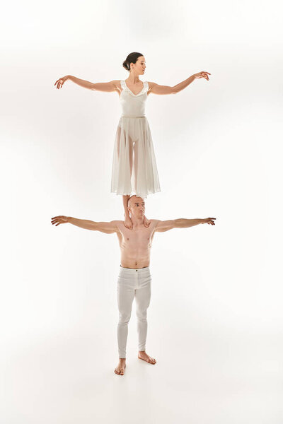 Shirtless young man and woman in white dress showcase acrobatic talent, balancing in a dynamic dance pose.