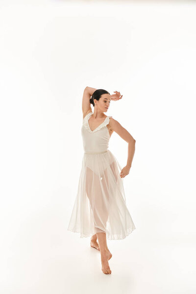 A graceful young woman in a flowing white dress sways and twirls in a studio setting against a white background.