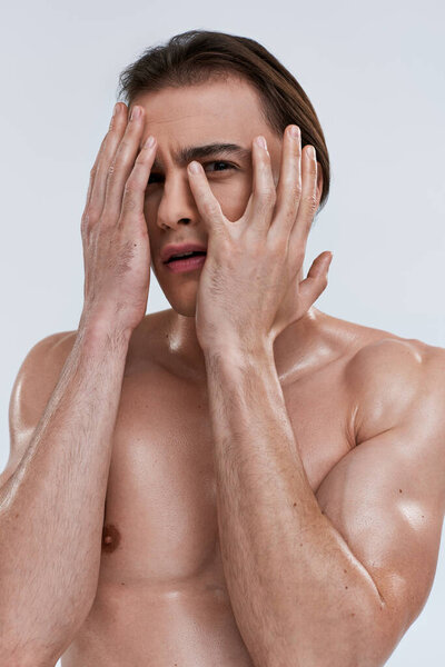 красивый испуганный мужчина без рубашки позирует эмоционально на сером фоне и смотрит прямо в камеру