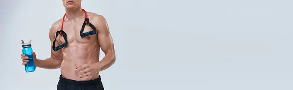 stock image cropped view of sporty man in black pants posing topless with bottle and fitness expander, banner