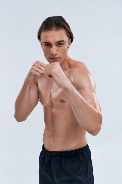 handsome sexy sporty man in black pants posing topless with fists in front of him looking at camera