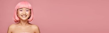 Canlı arkaplanda pembe saçlı ve makyajlı mutlu ve çekici Asyalı kızın yatay görüntüsü.