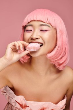 Çekici Asyalı genç kadın pembe saçlı ve gözleri kapalı canlı arka planda mochi yiyor.