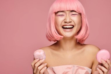 attractive asian woman in 20s with pink hair happy laughing and holding sweets on vibrant background clipart