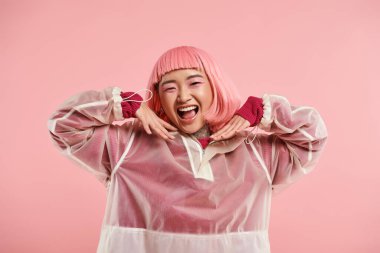 20 'li yaşlarda güzel Asyalı bir kadın pembe saçlı ve makyajlı mutlu, elleri parlak arka planda gülümsüyor.