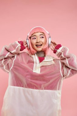 Pembe saçlı tatlı Asyalı genç kız kulaklıkla canlı arka planda müzik dinliyor.