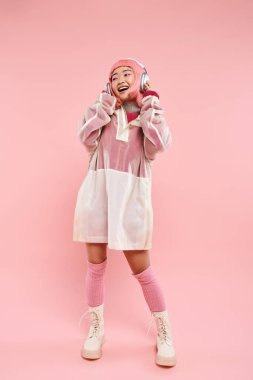 Pembe saçlı mutlu Asyalı genç bir kadın kulaklıkla canlı arka planda müzik dinliyor.