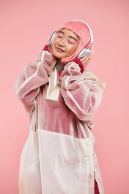 20 'li yaşlarda, güzel Asyalı bir kadın. Gözleri kapalı, kulaklıklı, canlı arka planda müzik dinliyor.