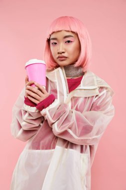 Pembe saçlı, kendine güvenen Asyalı genç bir kadın hayat dolu arka planda kahve fincanıyla poz veriyor.