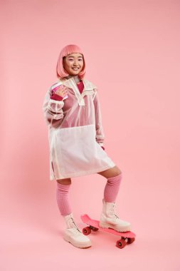 Pembe giysili mutlu bir kadın. Bir fincan kahve ve kaykayla poz veriyor.