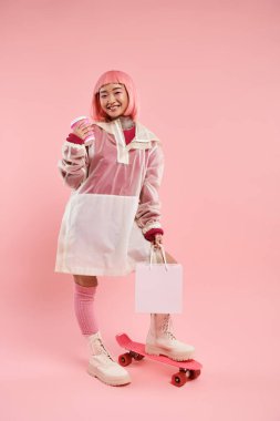 Bir fincan kahve, alışveriş paketi ve canlı arka planda kaykayla poz veren sevimli Asyalı kadın.