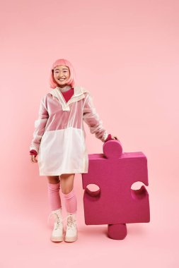 Pembe saçlı tatlı Asyalı genç kız, parlak arka planda büyük bir bulmacayla poz veriyor.