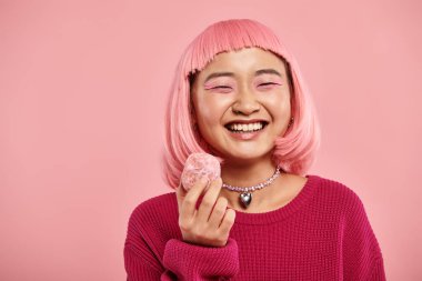 Mutlu Asyalı genç kadın gülümsüyor ve ellerini pembe arka planda tutuyor.