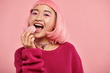 Pembe saçlı, neşeli Asyalı kadının portresi canlı arka planda hayranlıkla mochi yiyor.