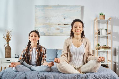 A mother and daughter bond as they practice yoga together on a cozy bed at home, fostering connection and wellness. clipart