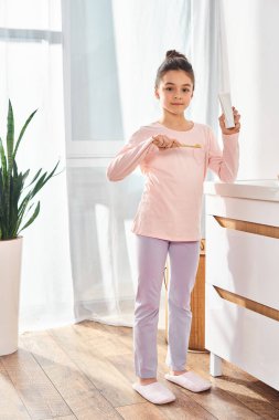 Modern bir banyoda diş fırçası tutan bir kız, hijyen rutininin önemini vurguluyor..